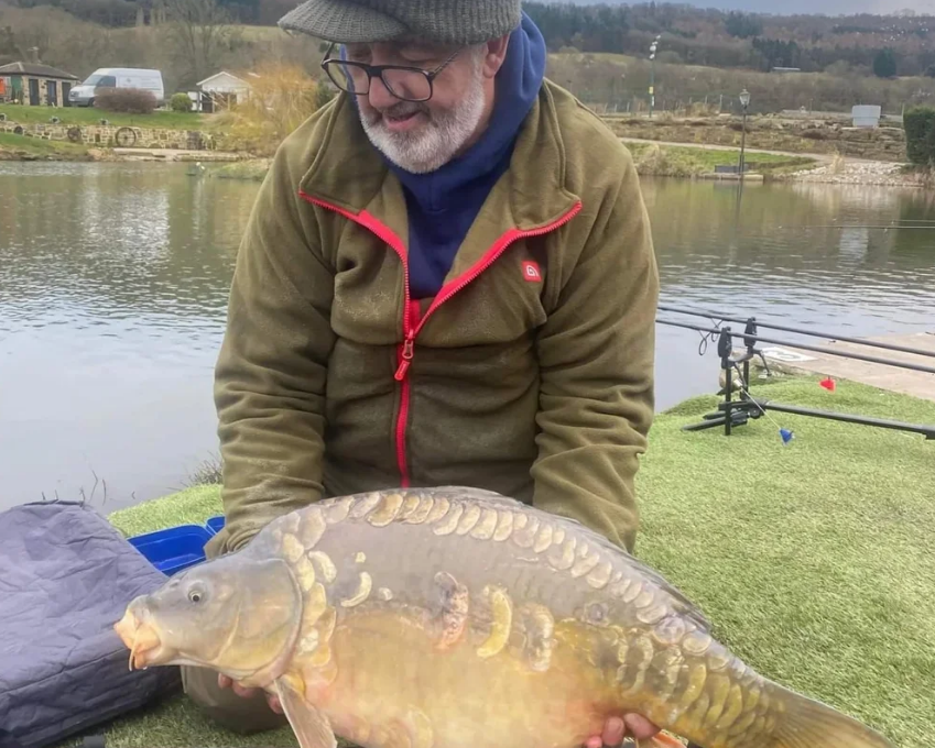 Angler holding a carp beside the fishing water