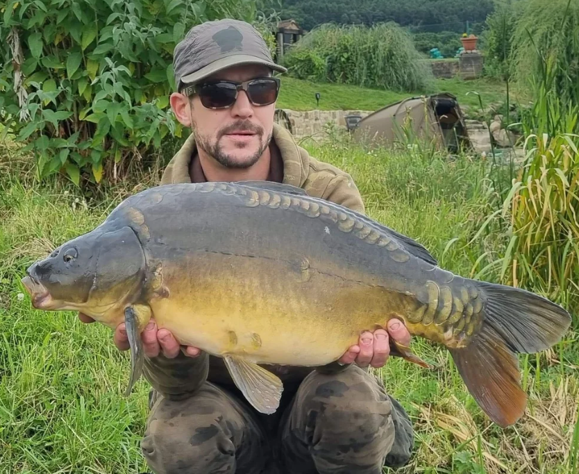 Crouching angler holding a mirror carp beside a bivvy