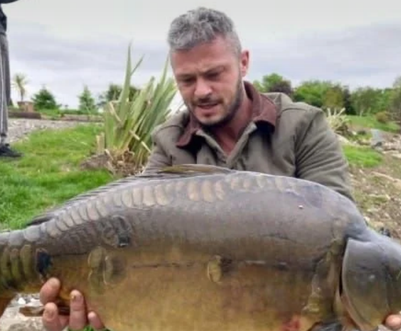 Angler holding a heavy mirror carp in front of tall reeds