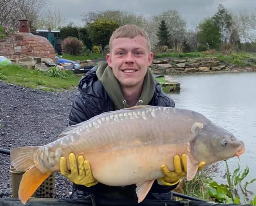 Young angler holding a mirror carp at the water’s edge